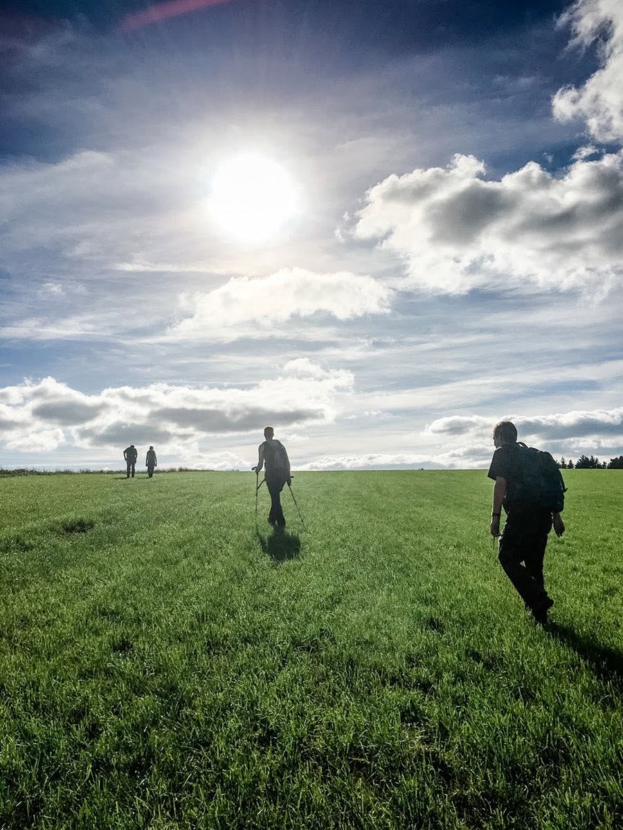 Walkers crossing open grassland on a sunny ridge near Kington